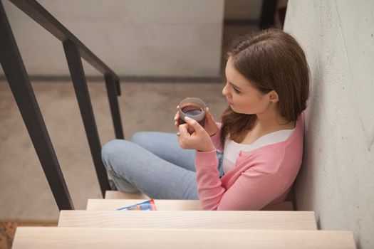 Top view shot of a beautiful woman drinking tea, sitting on the stairs at her apartment