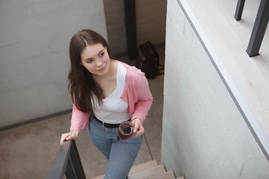 Top view shot of a beautiful woman walking up the stairs with a cup of tea at her hotel room or apartment