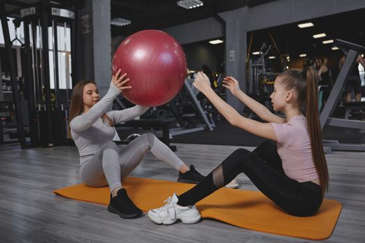 Young girl exercising with her personal trainer, using fit ball, doing abs exercise
