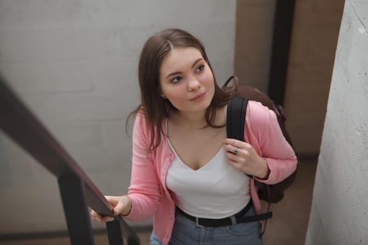 Beautiful young woman carrying backpack, walking up the stairs