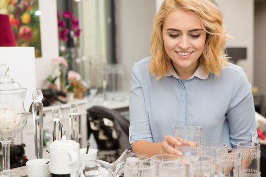 Happy young beautiful woman smiling joyfully choosing glassware at the local store copyspace houseware dinnerware champagne housewife buyer customer consumer shopper shopaholic lifestyle