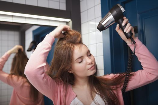 Close up of a beautiful relaxed woman enjoying blow drying her hair