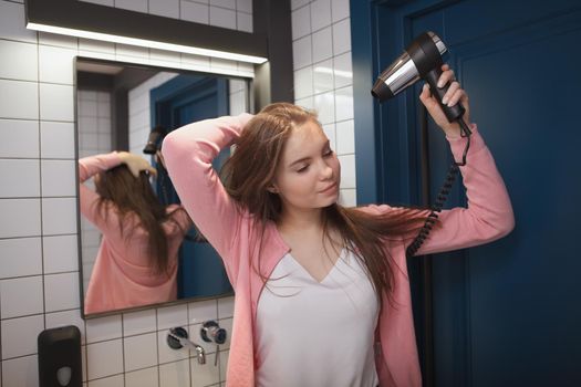 Charming young woman blow drying her hair in the bathroom