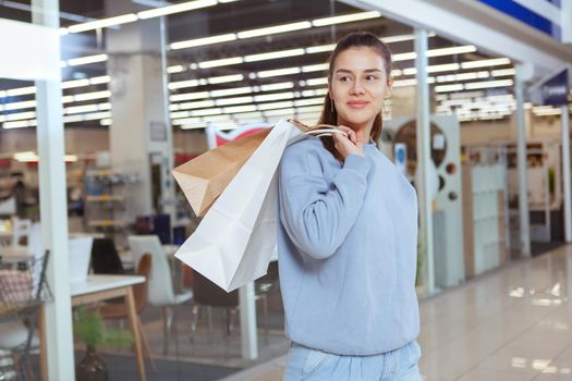 Happy young woman smiling, looking away cheerfully, carrying shopping bags at the mall