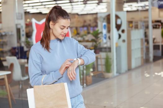 Young beautiful woman using her smart watch while shopping at the mall, copy space