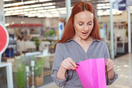 Lovely mature woman looking excited, opening her shopping bag at the mall. Female customer looking inside her shopping bag