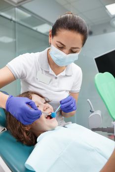 Vertical shot of a female dentist working at her clinic, treating teeth of young boy