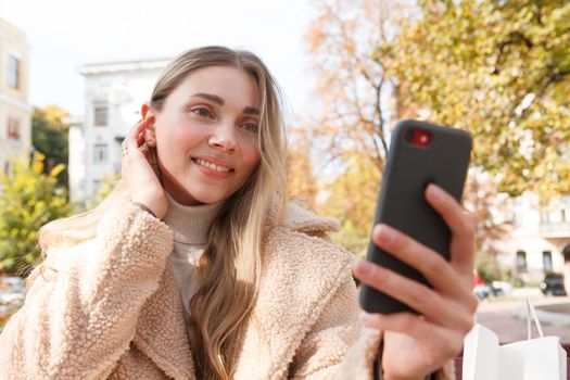 Charming woman smiling, taking selfies with her smart phone outdoors on a sunny autumn day