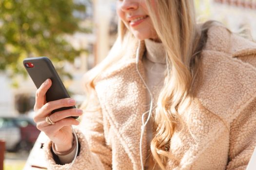 Cropped shot of a woman using smart phone with earphones outdoors