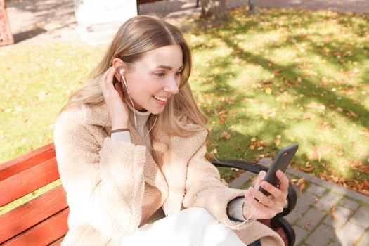 Happy woman wearing earphones, using her smart phone outdoors