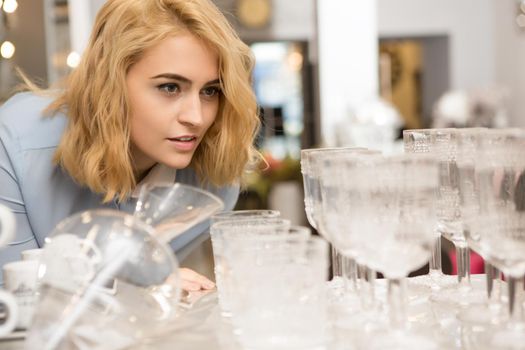 Attractive young woman looking at glassware display at the local houseware store shopping for home accessories dinnerware glassware buying luxury consumerism purchase sale retail discount offer price