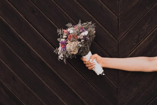 Wedding bouquet in bride's hands on wooden plank background