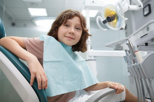 Charming young boy smiling to the camera, sitting in dental chair