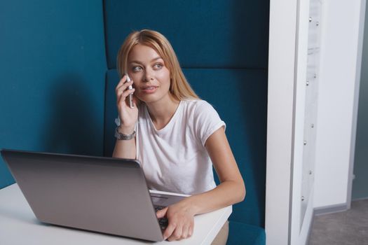 Happy beautiful woman talking on the phone, working on laptop in a modern workspace