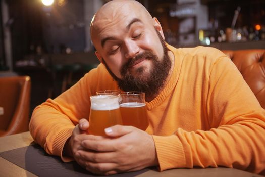 Charming young man smiling with his eyec closed embracing beer mugs. Happy man hugging beer glasses