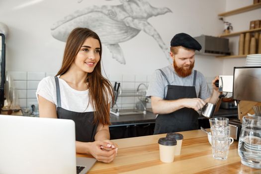 Coffee Business Concept - Positive young bearded man and beautiful attractive lady barista couple enjoy working together at the modern coffee shop