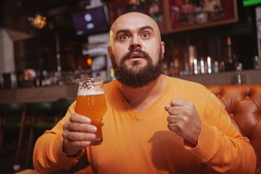 Attractive man watching football game at sports bar, holding beer in his hand