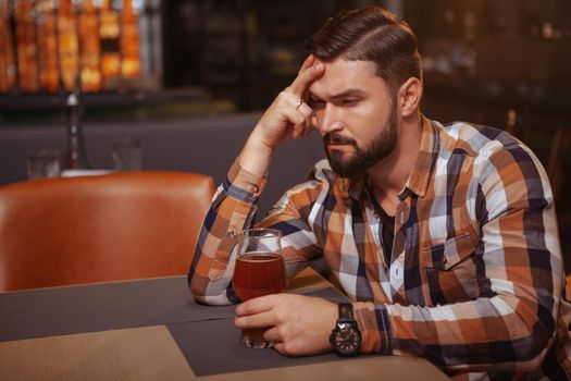 Depressed young man drinking alone at the bar. Handsome man looking drunk, sitting alone at the bar with a glass of beer