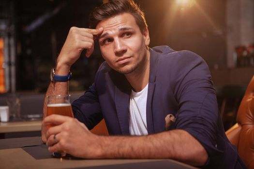 Handsome businessman drinking beer at the pub, looking away thoughtfully