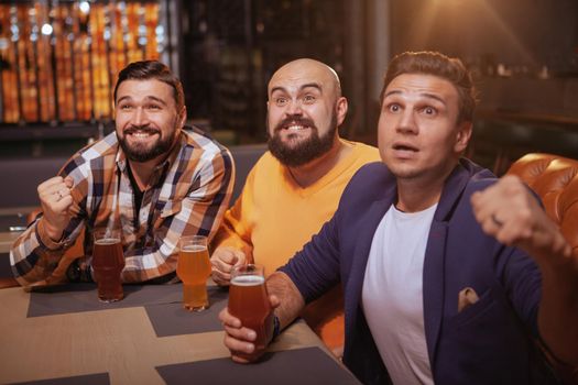 Group of male soccer fans watching a game at sports bar, drinking beer. Men screaming while watching football match at beer pub