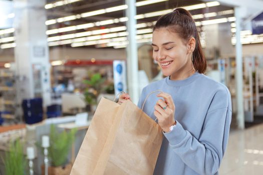 Young attractive woman looking excited, opening her shopping bag. Happy female customer looking inside her shopping bag