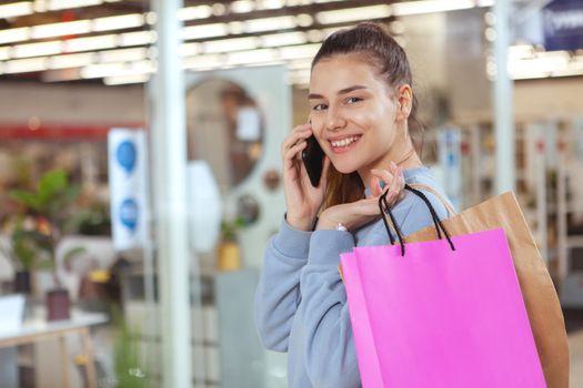 Attractive young woman carrying shopping bags at the mall, talking on the phone, copy space