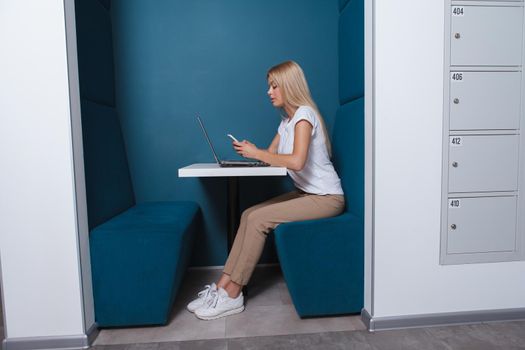 Full length shot of a female student using smart phone and laptop in modern university workspace