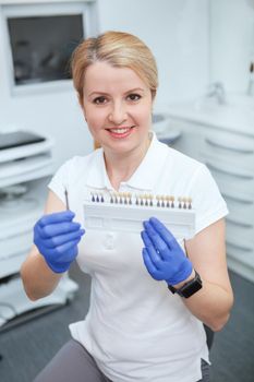 Vertical shot of a cheerful female dentist holding teeth whitening shade guide