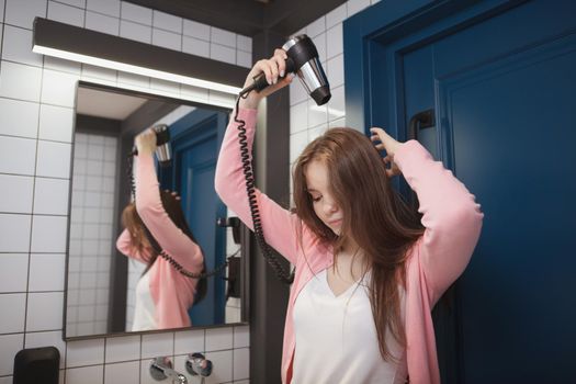 Long haired woman using blow dryer at the hotel room bathroom