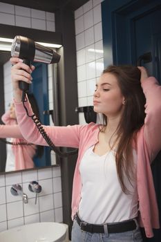 Vertical shot of a beautiful woman blow drying her hair at the hotel room