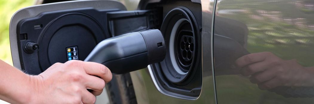 A man holds a pipe for refueling an electric car, close-up. Alternative safe fuel, electric refueling. Green energy, clean ecology