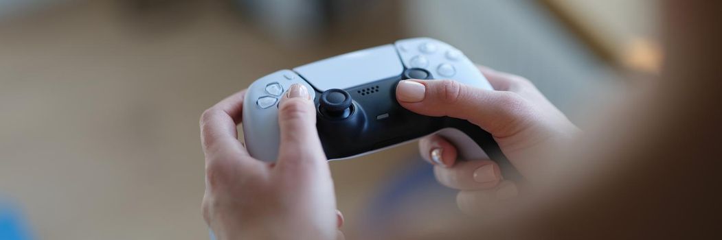 Female hands are holding a gaming gray joystick, close-up. Game addiction, gamer's device. Playstation, gadget