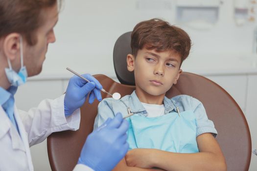 Cropped shot of young boy refusing to open his mouth for the dental checkup. Unhappy little boy refusing to get caries treatment by professional dentist