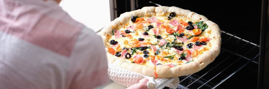 Woman in the kitchen bakes pizza in the oven, close-up. Homemade food preparation, traditional italian appetizer