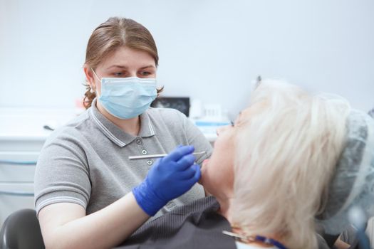 Female dentist wearing medical face mask, examining teeth of senior patient