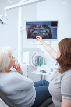 Vertical shot of a senior woman and her dentist looking together at dental x-ray scan