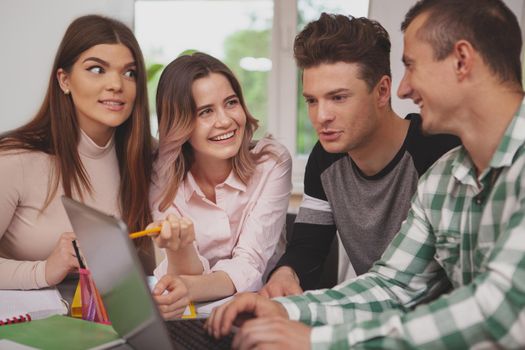 Cropped shot of happy young college students laughing, discussing their project. Beautiful young female student smiling, talking to her classmates, studying at the library