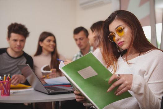 Concentration, achivement concept. Beautiful female university student reading assignment in her textbook, her classmates working on a project on the background, copy space