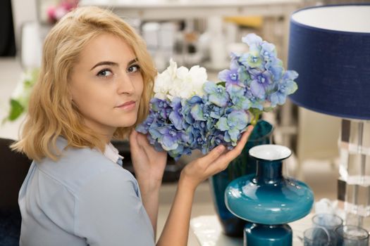 Young gorgeous blonde woman smiling to the camera over her shoulder holding beautiful hortensia flowers decorating her cozy home lifestyle lesire designer interior homeware relaxation floral