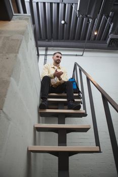 Vertical low angle shot of a bearded male tourist sitting on top of the staircase with his backpack at the hotel room