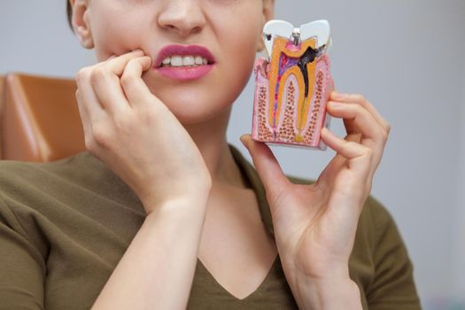 Cropped close up of a woman having toothache holding tooth mold with caries, copy space. Female patient waiting for dental treatment at the clinic. Dentist, health concept