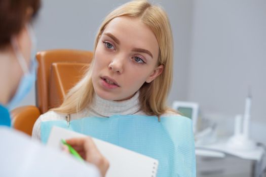 Young blond haired woman having medical consultation with professional dentist at the clinic, copy space. Beautiful woman talking to her dentist. Female patient visiting dentist. Helpful service
