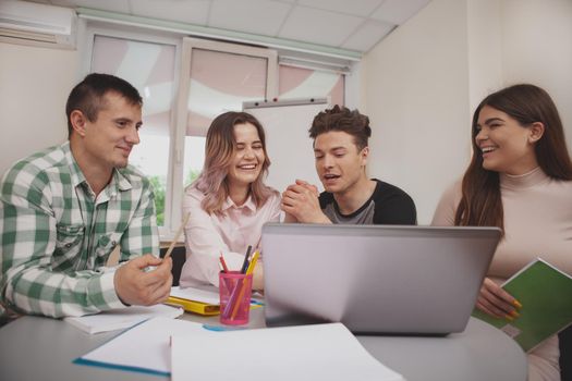 Diverse group of college friends studying together, using laptop. University students discussing their project at the classroom. Education, friendship concept