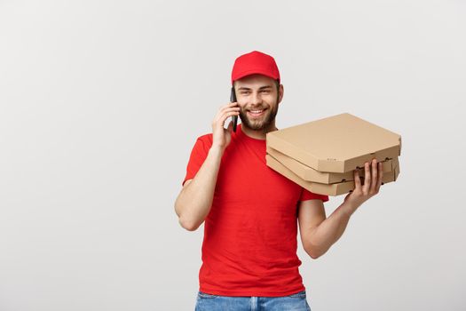 Portrait of a smiling delivery man in red cap talking on mobile phone while holding pizza boxes isolated on the white background.