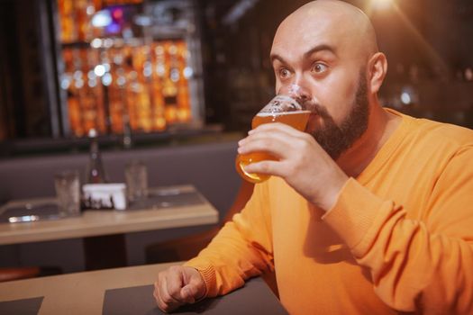 Bald man looking overwhelmed, drinking delicious beer at the pub. Mature man drinking tasty beer with pleasure