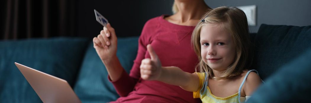 Mom and daughter pay by card for purchases sitting on the couch at home. Ordering goods at home during a pandemic, self-isolation