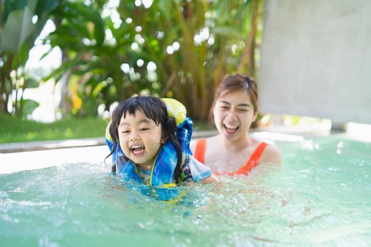 Mother and daughter swimming playing in the pool, smiling and laughing. Having fun in the pool at the resort hotel, family happy concept.