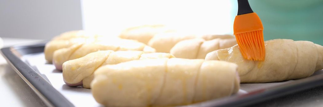 A woman is brushing dough products with a brush, close-up. Bakery making sausages in dough, cooking, fast food