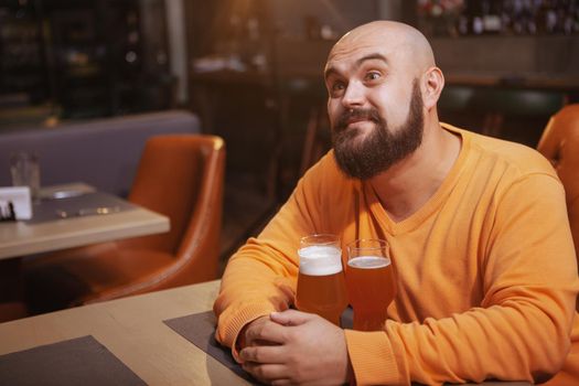 Charming young bearded man looking away dreamily hugging three glasses of various craft beer at the pub, copy space