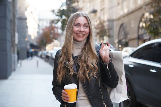 Charming happy woman carrying shopping bags in city center, having coffee on the go